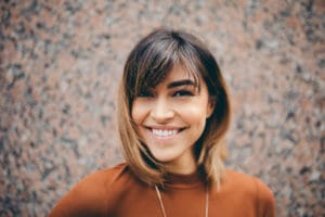 Portrait of a smiling woman's face with shoulder length hair wearing a burnt orange sweater.