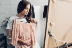 Breast Augmentation for Uneven Breasts. Woman trying on a blouse and looking in the mirror at home.