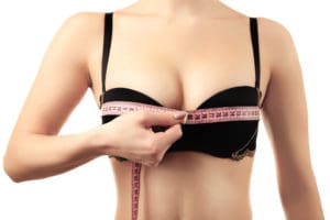 Woman in a black bra measuring around her breasts to help pick the right breast implant.