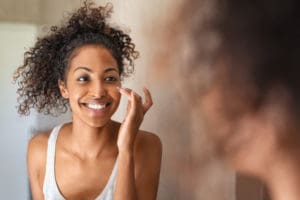 Woman looking into her bathroom mirror applying eye cream to help get rid of her puffy eyes.